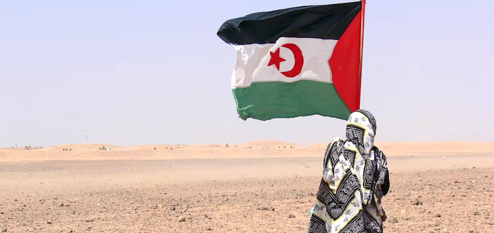 Una persona sostiene una bandera de la República Árabe Saharaui Democrática ante el muro que separa el Sáhara Occidental de Marruecos. Shutterstock / Natalia de la Rubia