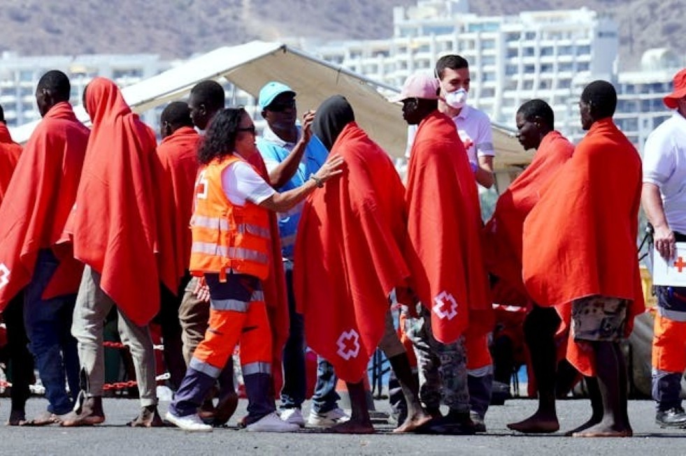 Migrantes usan mantas rojas para calentarse después de ser rescatados en el mar en el puerto de Arguineguín (Gran Canaria). Canary4stock/Shutterstock